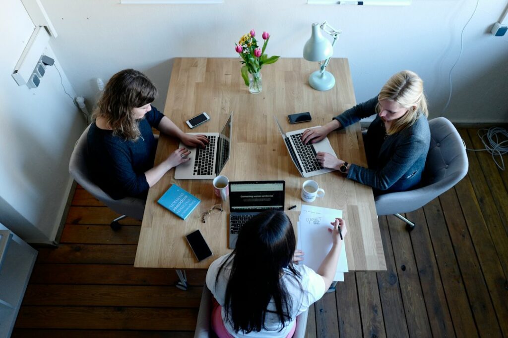 Symbolfoto: Drei Kolleginnen arbeiten gemeinsam an einem Tisch – Foto CoWomen auf Unsplash